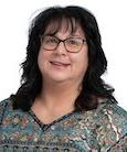 Headshot: Dark haired woman in paisley top and glasses smiling at the camera