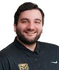 Headshot: Dark haired man in dark shirt and beard smiling at the camera